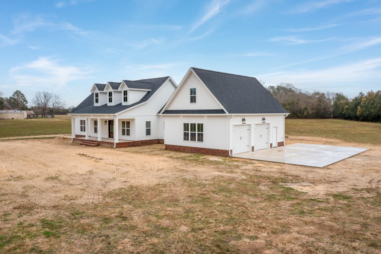 The Morgan Build: Custom white farmhouse with a side-load garage, brick foundation, and dormer windows on Neuse Road in Kinston, NC.
