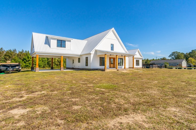 The Manning Build: Modern white farmhouse with a silver metal roof and wood-wrapped porch pillars on Casey Road by Signature Homes ENC.