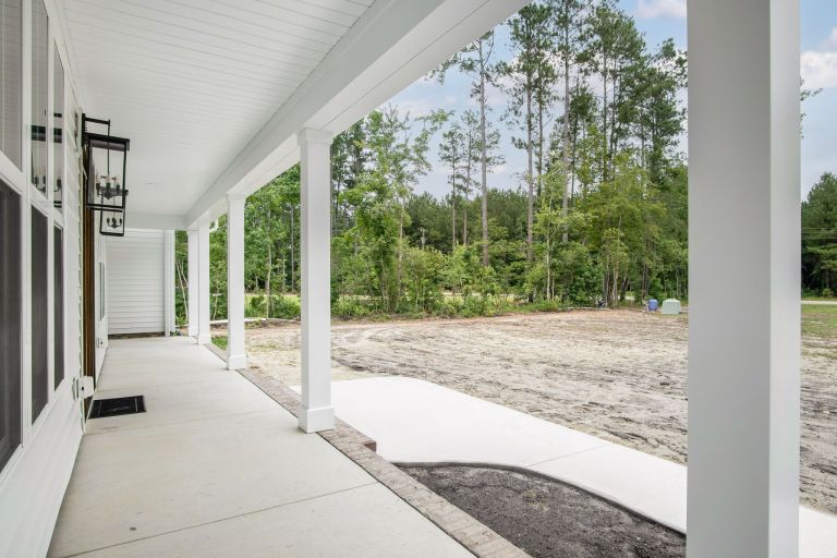 Long covered front porch with white columns and dark ceiling fan, offering a serene view of a wooded lot by Signature Homes.