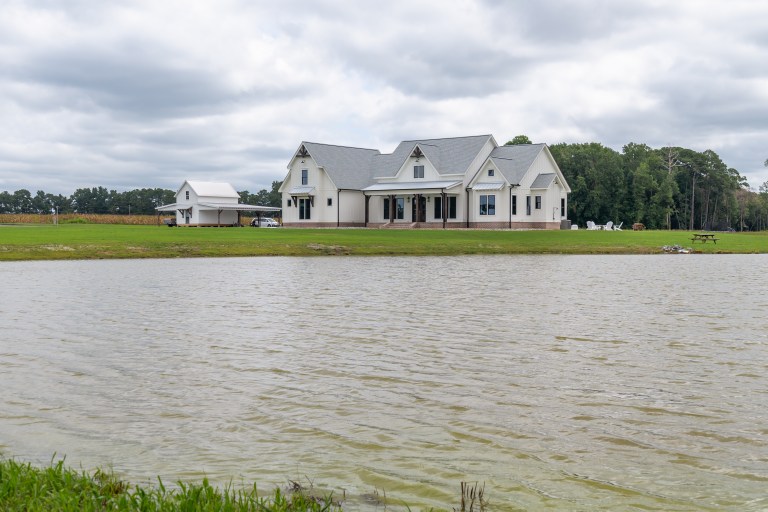 Custom modern farmhouse with white siding and black trim built by Signature Homes near a pond in Eastern North Carolina.